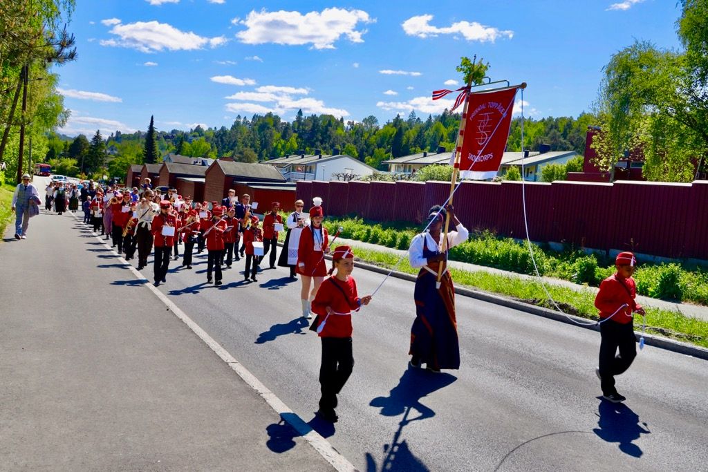 17. mai-toget med korps og faner på veien gjennom nabolaget